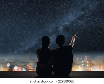 Die Silhouette der Paare sitzt in der Nacht auf dem Dach über der Stadt.