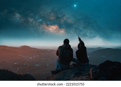 silhouette of a couple sitting on top of a hill looking at the stars over the city - Shutterstock ID 2221015755