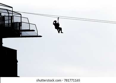 Silhouette Of Couple Tourists, Father And Son Wearing Are Playing Zip Line And Selfie With Tower With Blue Sky, Copy Space For Text. Idea Concept For Adventure Recreation.