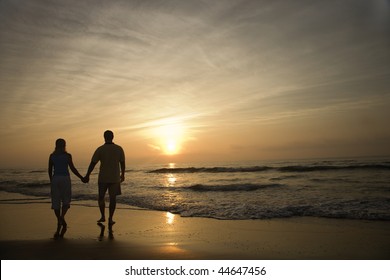Silhouette of couple walking on beach at sunset holding hands. Horizontally framed shot. - Powered by Shutterstock