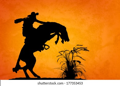 Silhouette Of Cowboy Reigning Bucking Bronco Spooked By Something In The Nearby Sagebrush. Sunset Orange/yellow Textured Background.
