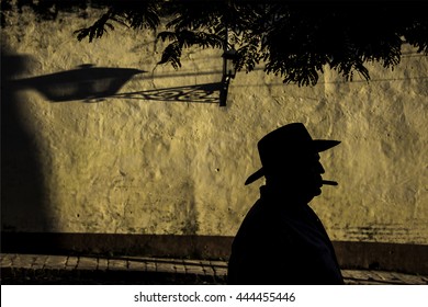 午後の遅い日差しに背景に、植民地のオレンジ色の建物を持つ葉巻を吸うキューバのカウボーイのシルエットと、長い影を持つ古い植民地のランプ。