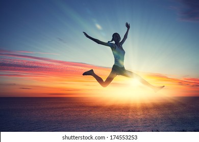 Silhouette of dancer jumping against city in lights of sunrise