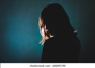silhouette of depress woman standing in the dark with light shine behind