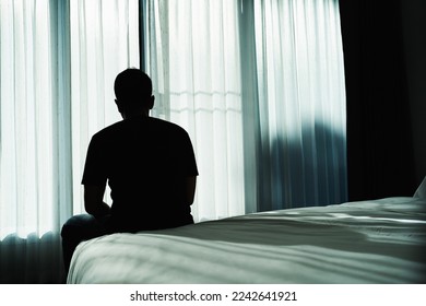 Silhouette depressed man sadly sitting on the bed in the bedroom. Sad asian man suffering depression insomnia awake and sit alone on the bed in bedroom. Depression health people concept.