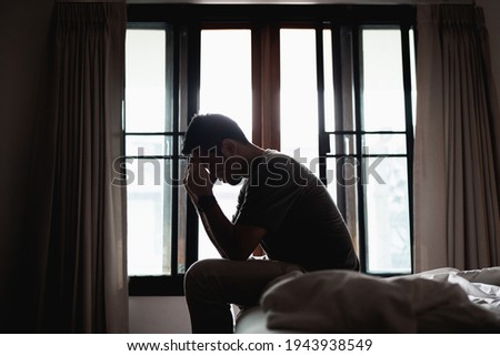 Silhouette depressed man sadly sitting on the bed in the bedroom, depression concept