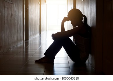 Silhouette of depressed woman head bending touch her hand sitting lean against the wall  - Powered by Shutterstock