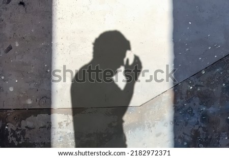 The silhouette of a desperate man, his hands raised in front of the face, projected by the sunlight on the wall of an old abandoned house. Dust floating in the air creating an eerie feeling.
