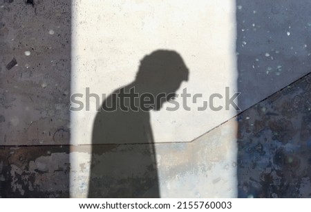 The silhouette of a desperate man, sad and surrendering, projected by the sunlight on the wall of an old abandoned house. Dust floating in the air creating an eerie feeling.