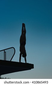 Silhouette of diver in handstand, preparing to dive from platform. Photographed at dusk