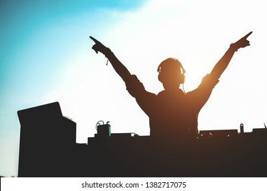 Silhouette of dj mixing outdoor with hands up at sunset - Portrait of disc jockey playing old style vinyl music for people on beach party - Fun, summer, entertainment and fest concept - Focus on him