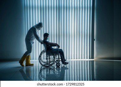 Silhouette of doctor in hazmat suit pushing coronavirus patient on wheelchair near the window - Powered by Shutterstock