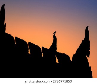 Silhouette of dramatic temple's rooftop with a bird perched on the peak against a colorful orange and blue sunset sky. Minimalist nature scene symbolizing freedom, solitude, and tranquility.