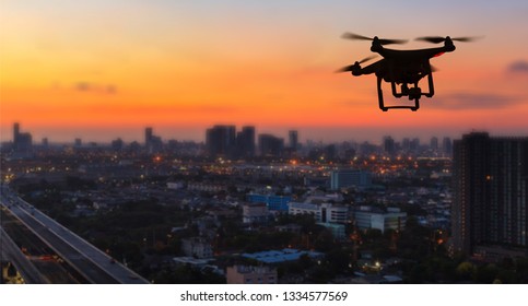 Silhouette Of Drone Flying Above City At Sunset