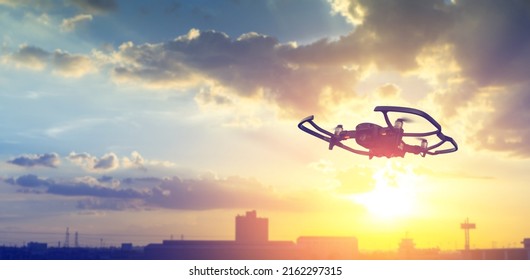 Silhouette drone flying overhead in cloudy sunset city sky.