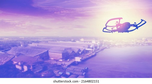 Silhouette drone flying overhead factory and warehouse at sunset sky.