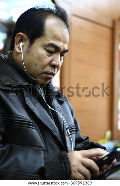\
Silhouette edge Asian man sitting \
listening to music from smartphone\
in-Thailand.