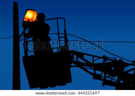 Silhouette electrical engineer is repairing on a light pole on the blue sky background
