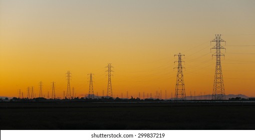 Silhouette of electrical power transmission pylons under sunset golden sky. The photo was taken at Baylands Nature Preserve in Palo Alto, California, by the south end of the San Francisco Bay.