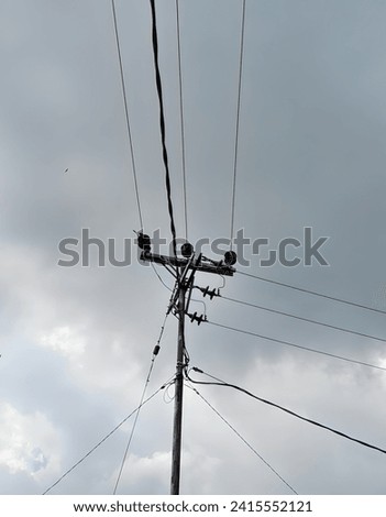 Silhouette of an electricity pole with chaotic cables, photographed in the afternoon from below