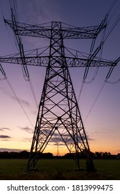 Silhouette Of Electricity Tower Construction And Power Lines Against A Colourful Orange And Magenta Blue Purple Sunset Sky