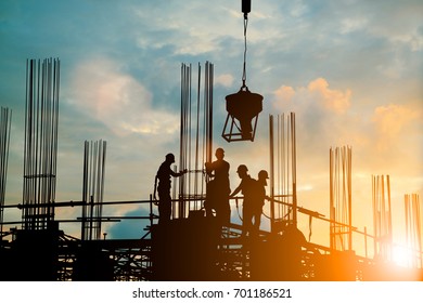 Silhouette Of Engineer And Construction Team Working Safely Work Load Concrete On Scaffolding On High Rise Building. Over Blurred Background Sunset Pastel For Industry Background With Light Fair 