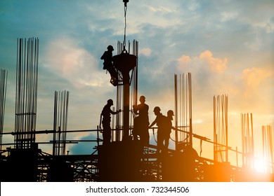 Silhouette Of Engineer And Construction Team Working Safely Work Load Concrete On Scaffolding On High Rise Building. Over Blurred Background Sunset Pastel For Industry Background With Light Fair 