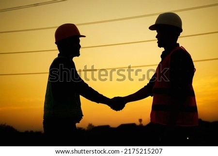 Silhouette of Engineer and foreman worker shaking hands at construction site during sunset