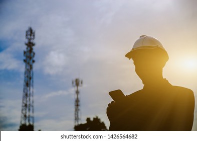 Silhouette of Engineer holding a mobile phone with telecommunication antenna and sunset background.