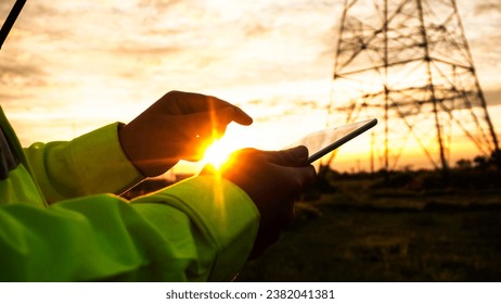 Silhouette of engineer man using tablet checking high-voltage power lines.