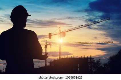 Silhouette engineer standing survey work on construction over blurred Worker in  construction site and sunset.