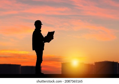 Silhouette of Engineer under inspection and checking oil storage tank, Engineer man in waistcoats and hardhats and with documents in oil storage plant