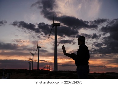 Стоковая фотография: Silhouette of engineer working on laptop at wind farm