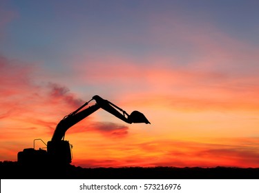 silhouette of Excavator loader at construction site with raised bucket over sunset