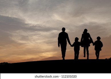 Silhouette Of A Family Comprising A Father, Mother And Two Children Walking Into The Sunset.