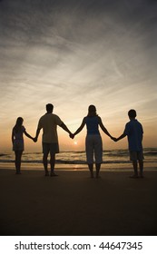 Silhouette Of Family Holding Hands On Beach Watching The Sunset. Vertically Framed Shot.