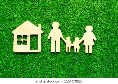 Silhouette Of Family, House Made Of Wood On The Background Of Artificial Green Grass Covering For Landscape Design. Family Values, Real Estate.