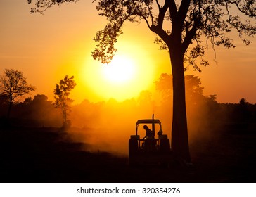 Silhouette farmer with tractor on the farm are working in hot colors of the evening light .