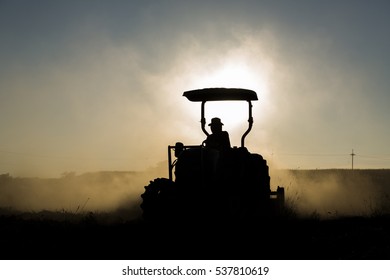 Silhouette farmer with tractor is working in the farm at dusk