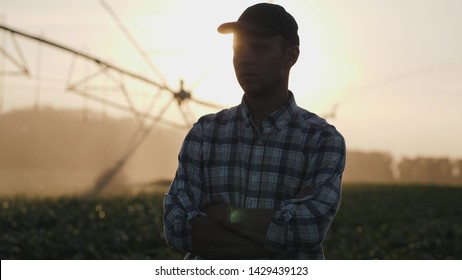 Silhouette of a farmer watching the irrigation of a cornfield using the center pivot sprinkler system at sunset