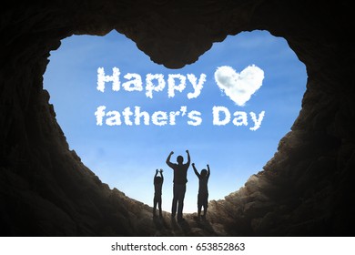 Silhouette Of Father And Children Lifting Hands In A Cave While Looking At Clouds Shaped Happy Father's Day Word On Sky 