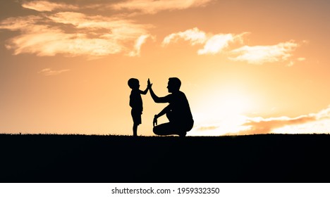 Silhouette of father giving his son high five in the park. Parenting, fatherhood, and happy childhood concept. 
