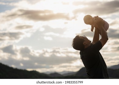 Silhouette Father Raises His Daughter Is Not Yet A Year Old Lift Up In The Sky. Father Holding Daughter In Arms. Happy Asian Family Child And Dad Walking Outdoor Nature. Happy Father's Day