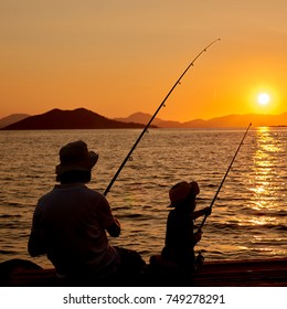 Silhouette of father and son or boy and man, fishing on wooden pier at sunset