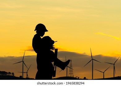 Silhouette Of Father And Son With Clipping Path In Hard Hat, Happy Dad Carrying Son On Shoulders Checking Project At Wind Farm Site On Sunset In Evening Time