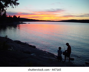 Silhouette Of Father And Son Fishing At Sunset