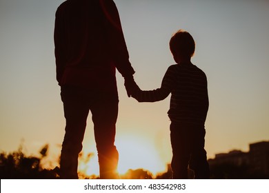 silhouette of father and son holding hands at sunset