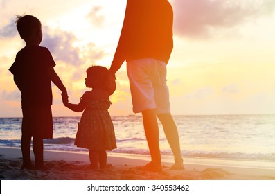 Silhouette Of Father And Two Kids Walking On Beach At Sunset