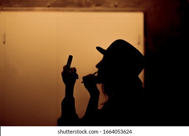 Silhouette Of A Female Actress In A Hat Who Paints Her Lips And Looks In The Mirror Backstage On A Yellow Background.