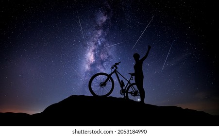 Silhouette FeMale And Bike On Rock With Blue Night Sky Milky Way And Shooting Stars On Dark Background.with Noise And Grain.